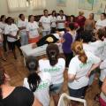 Mulheres observam profissional em simulação de cuidado com pessoa acamada numa maca. #paratodosverem