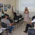 Professora, com máscara de proteção, dá aula para vários alunos sentados. #paratodosverem