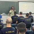 Mulher está em pé falando a um grupo de guardas que estão sentados em sala de aula. #paratodosveram