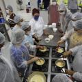 pessoas de pé mexendo em panelas sobre fogão industrial. Trata-se de uma aula de culinária. #paratodosverem