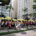 pessoas caminham no calçadão da orla com guarda-chuvas amarelos. #paratodosverem