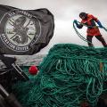 cena do documentário. Homem está em cima de barco, puxando uma imensa corda. Ao lado dele, uma bandeira da Sea Shepperd. #paratodosverem