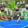Três jovens seguram terra e local de compostagem #paratodosverem