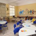 Interior de classe com pintura artística nas paredes. Mesas e cadeiras. #paratodosverem