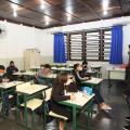alunos estão sentados em carteiras. Professora na frente de todos. #paratodosverem
