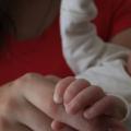 bebê está no colo de uma mulher. mãozinha do bebê está segurando um dedo dessa mulher. foto em close. #paratodosverem