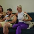 família está sentada no sofá. Mãe com um cachorrinho, e seus dois filhos adultos. O bebê está no colo do rapaz. #paratodosverem