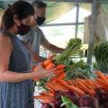Homem e mulher manuseiam cenouras expostas em barraca. #pracegover
