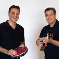 dois homens estão lado a lado. Um toca pandeiro e o outro, cavaquinho