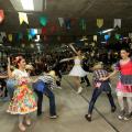 bailarinos dançam quadrilha junina com pessoas assistindo ao fundo #paratodosverem