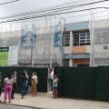visitantes estão parados em porta de escola coberta por manta de proteção porque a fachada está em obras. #paratodosverem