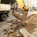 Escavadeira recolhe trecho de calçada demolido. Ao fundo se vê um desvio no trânsito. #paratodosverem