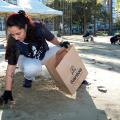 mulher está agachada na faixa de areia recolhendo microlixo e depositando em saco de papel. #paratodosverem