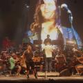 Músicos estão à frente da sinfônica e do maestro. #paratodosverem