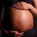 imagem em close de barriga de gestante com as mãos da mulher, uma abaixo e outra acima da barriga. #paratodosverem