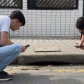 dois jovens observam buraco em rua. #paratodosverem 