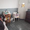 quarto com cama à esquerda (vê-se parcialmente), mesa de canto, cadeira e uma cômoda. #paratodosverem