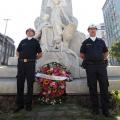 guardas municipais estão em pé diante de monumento a Braz Cubas e ao lado de coroa de flores. #paratodoverem