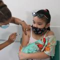 Mulher está vacinando menina. Ambas usam máscara. #paratodosverem
