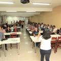 mulher de costas para a foto está falando a pessoas sentadas em uma sala de reuniões. #paratodosverem 