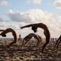bailarinas dançam na areia e tem o tronco curvado para trás em busca de atingir o chão com as mãos. #paratodosverem