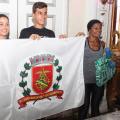 três corredores seguram bandeira com brasão de Santos #pracegover