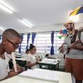 músico está em pé, com guarda chuva nas costas, tocando com aluno que está sentando tocando flauta #pracegover 