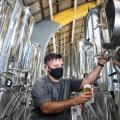 homem tira cerveja de equipamento na fábrica #paratodosverem
