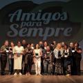 servidores reunidos no palco segurando medalhas posam para foto. Ao fundo, na parede se lê amigos para sempre. #paratodosverem