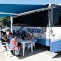 Ônibus do procon móvel está parado. Pessoas estão sentadas sendo atendidas por recepcionistas. #paratodosverem