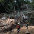 homens estão trabalhando em encosta onde foram instalados andaimes. #paratodosverem