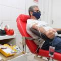 homem esta sentado em cadeira com apetrechos para doação de sangue. A bolsa já com quantidade do líquido está pendurada na cadeira. #paratodosverem