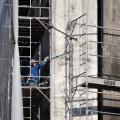 homem está em andaime reparando fachada de prédio. #paratodosverem 