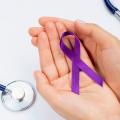 laço roxo sobre palma de mãos abertas e unidas. De um lado, um pedaço de um estetoscópio, do outro, uma caneta. #paratodosverem 