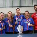 quatro atletas do tênis de mesa feminino seguram suas medalhas e posam atrás do troféu da Cidade. #paratodosverem