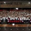 centenas de jovens uniformizados e em pé com as  mãos para o alto na plateia de teatro. #paratodosverem