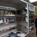 livros dispostos em biblioteca móvel. Uma mulher mexe em uma publicação. #paratodosverem