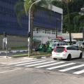 Semáforo em funcionamento em via. Há dois carros passando na pista sobre uma faixa de pedestres. #Pracegover