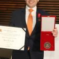 o jovem marcelo segura certificado com a mão direita e placa, com a direita 