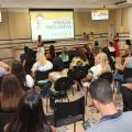 salão com várias pessoas sentadas assistindo a uma apresentação. Ao fundo, em um telão, se lê Virada Inclusiva. #paratodosverem