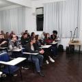 mulher está em pé falando a um grupo de pessoas sentadas. #paratodosverem 