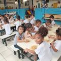 crianças sentadas comendo merenda escolar #paratodosverem