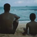 pai e filho olham para o mar em cena de filme #paratodosverem