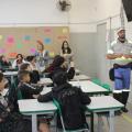 agente de trânsito está à frente de lousa em sala de aula e alunos estão assistindo. #paratodosverem