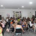 várias mulheres estão sentadas em volta de mesas fazendo artesanato. #paratodosverem