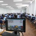 Computador com tela sobre projeto e crianças e prefeito ao fundo #paratodosverem
