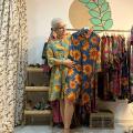 mulher segura peça de roupa colorida ao lado de arara com várias peças. #paratodosverem