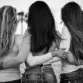 três mulheres de costas para a foto estão abraçadas. #paratodosverem