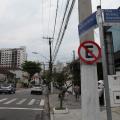 placa de proibido estacionar afixada em poste à direita. Carros passam pela rua. #paratodosverem