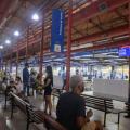 unidade do poupatempo, com pessoas sentadas em bancos. Ambiente é um antigo prédio restaurado, com estruturas aparentes e paineis indicando on